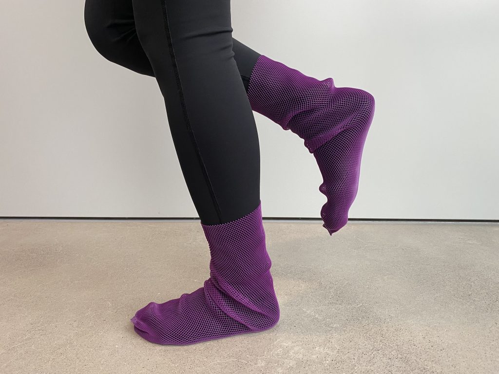 Musta housuinen nainen seisoo yhdellä jalalla violetit Pitosukat jalassaan